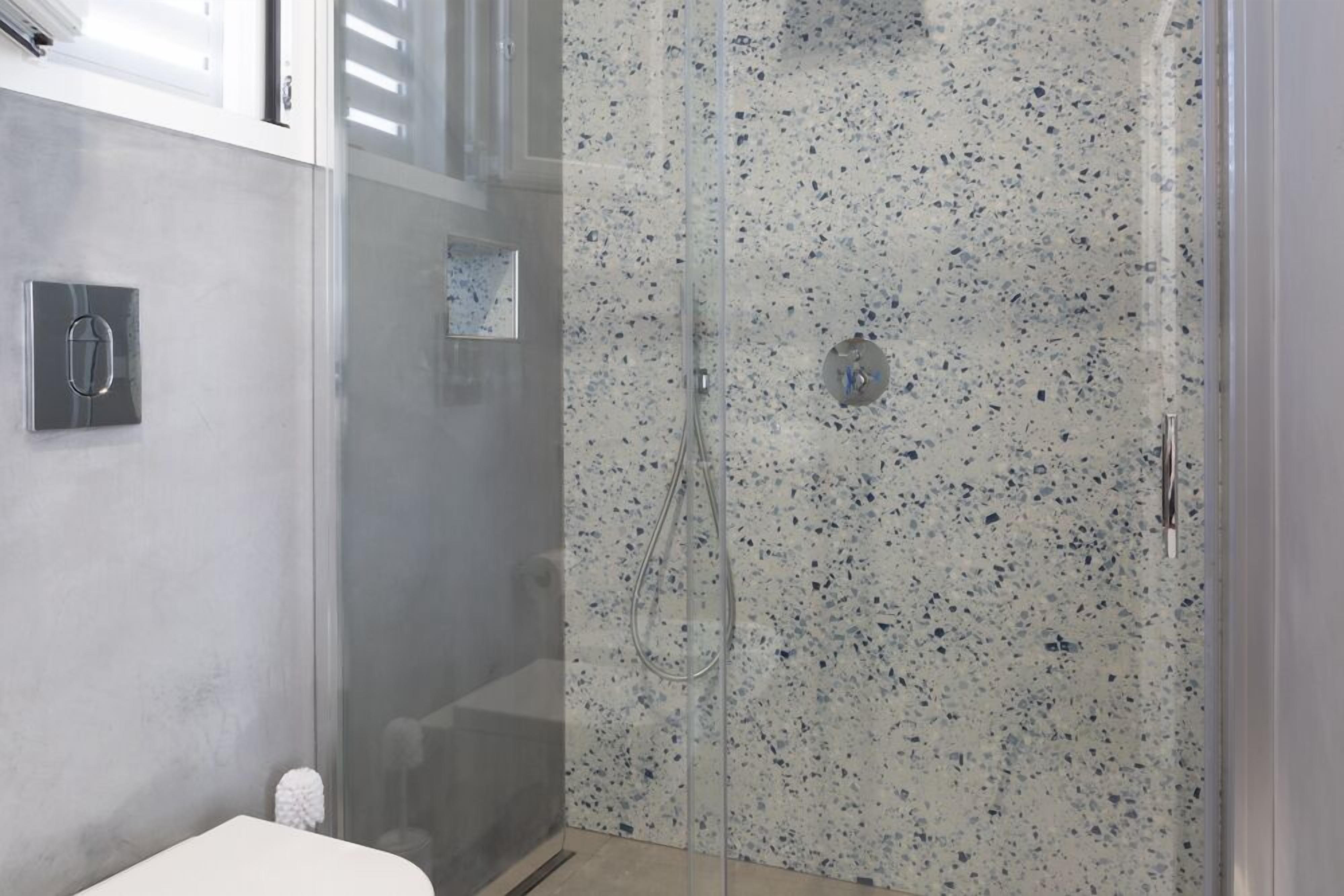A modern bathroom with a glass-enclosed shower, a white toilet, and a marble backsplash.