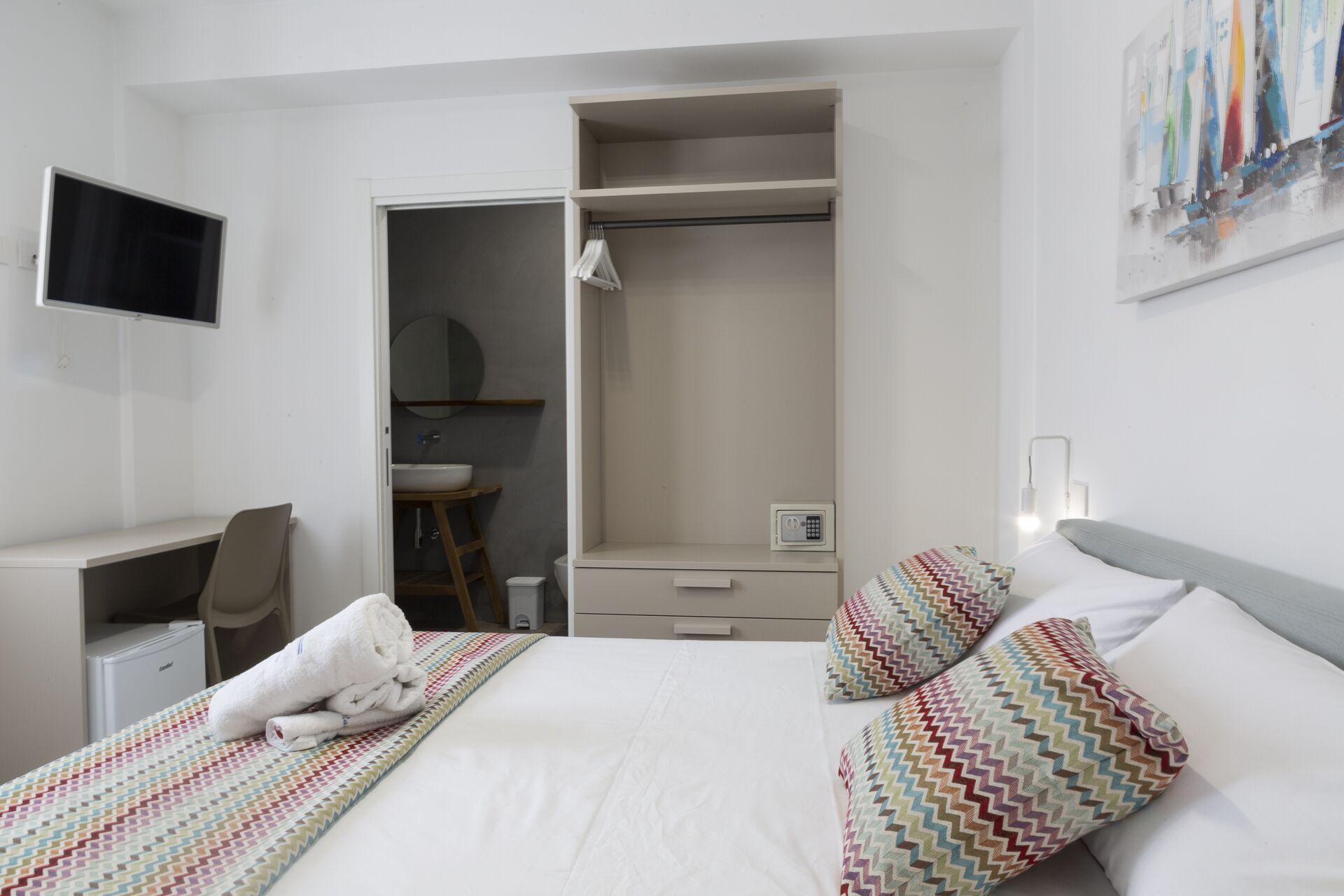A hotel room with a bed, a desk, a chair, a wardrobe, and a bathroom.