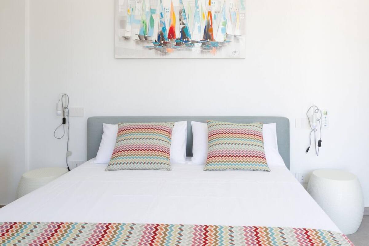 A neatly arranged bedroom with a bed, two pillows, a bedside table, and a wall-mounted artwork.