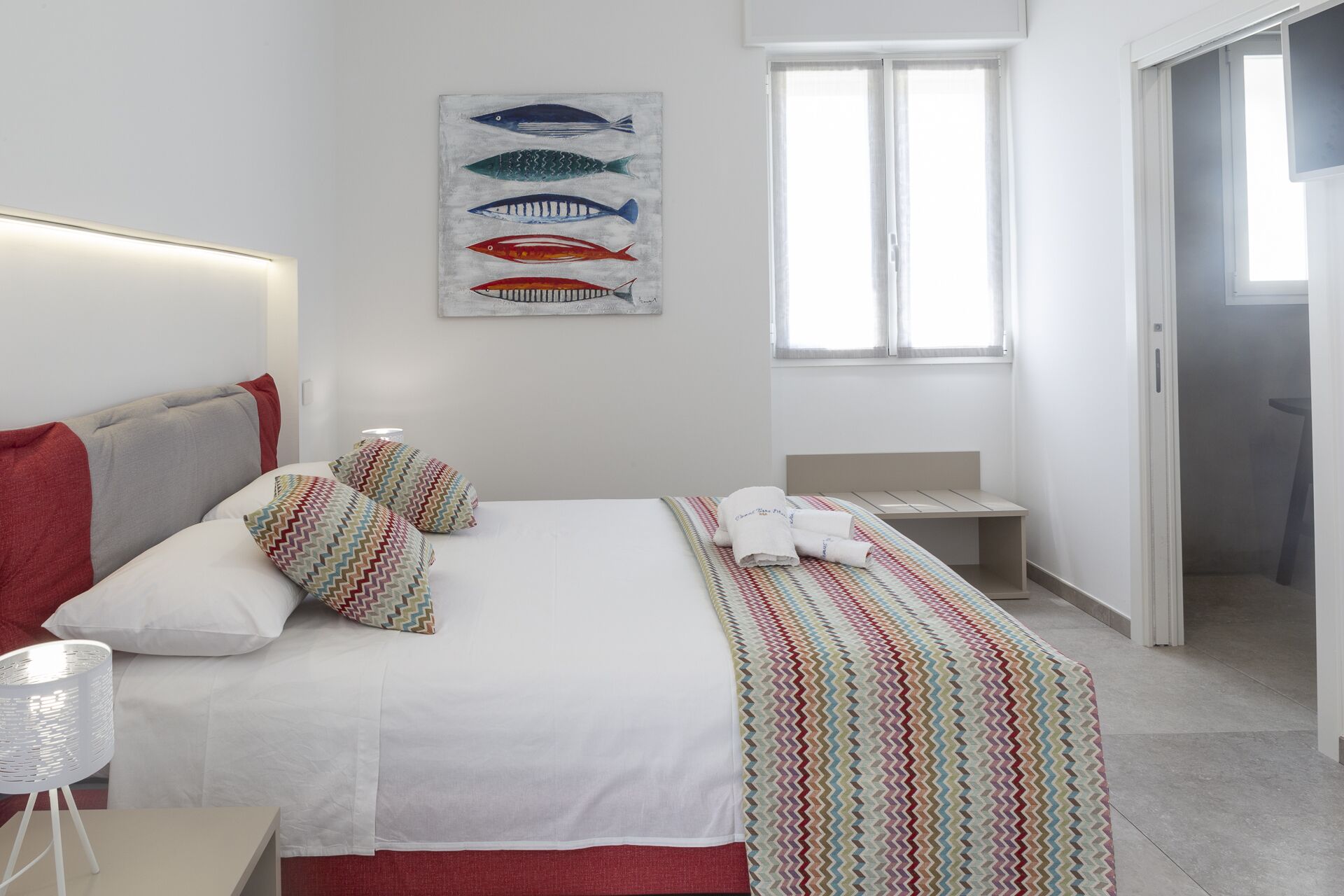 Ein Hotelzimmer mit Bett, Nachttisch, Lampe, Fenster und Tür.