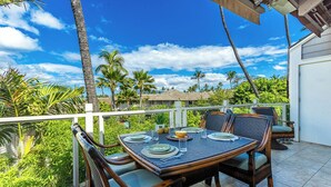 An outdoor dining area with a table set for four, surrounded by wicker chairs with cushions.