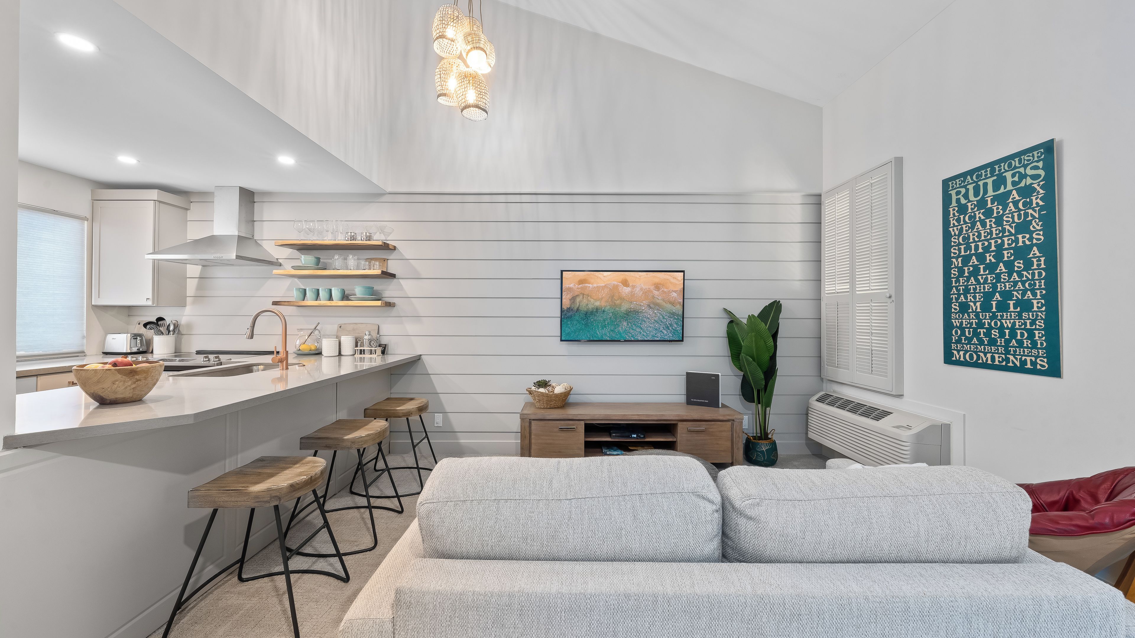 A modern kitchen with a central island, bar stools, and a dining area with a sofa.