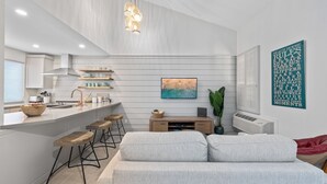 Une cuisine moderne dotée d’un îlot central, de tabourets en bois et d’un luminaire suspendu.