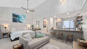 Une chambre moderne avec un grand lit, un canapé gris et un ventilateur de plafond.
