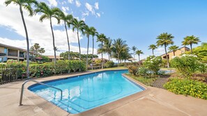 Une piscine à l’eau d’un bleu cristallin, entourée de palmiers et d’un jardin bien entretenu.