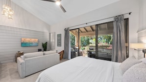Une chambre moderne avec un grand lit, un canapé, une télévision et une porte-fenêtre coulissante donnant sur un balcon agrémenté de plantes.