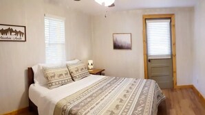 Una camera da letto con un letto, un comodino, una lampada, una porta e una parete con un quadro.
