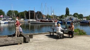 Un port de plaisance avec des bateaux amarrés, une promenade en béton et des personnes assises sur des bancs.