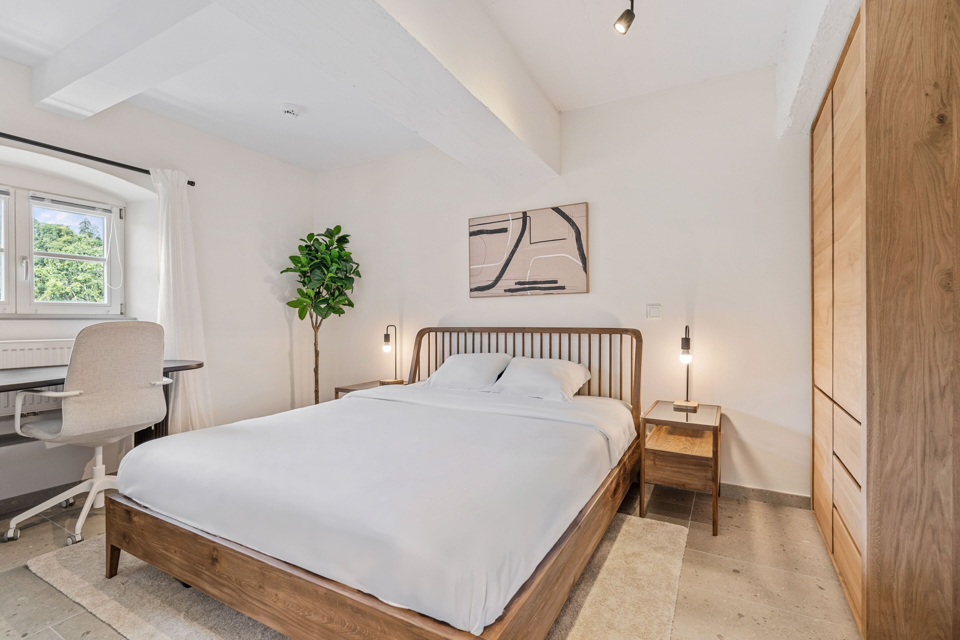 Una camera da letto con un letto in legno, una scrivania con una sedia, una pianta in vaso e un’opera d’arte appesa al muro.