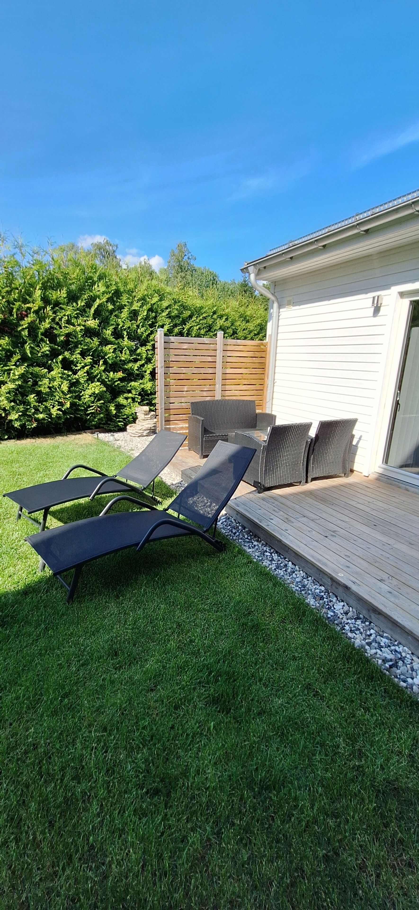 A backyard with two lounge chairs, a wooden deck, and a white building with a garage.