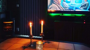 Quarto com televisão exibindo cena de filme, lareira com duas velas acesas e piso de azulejos.