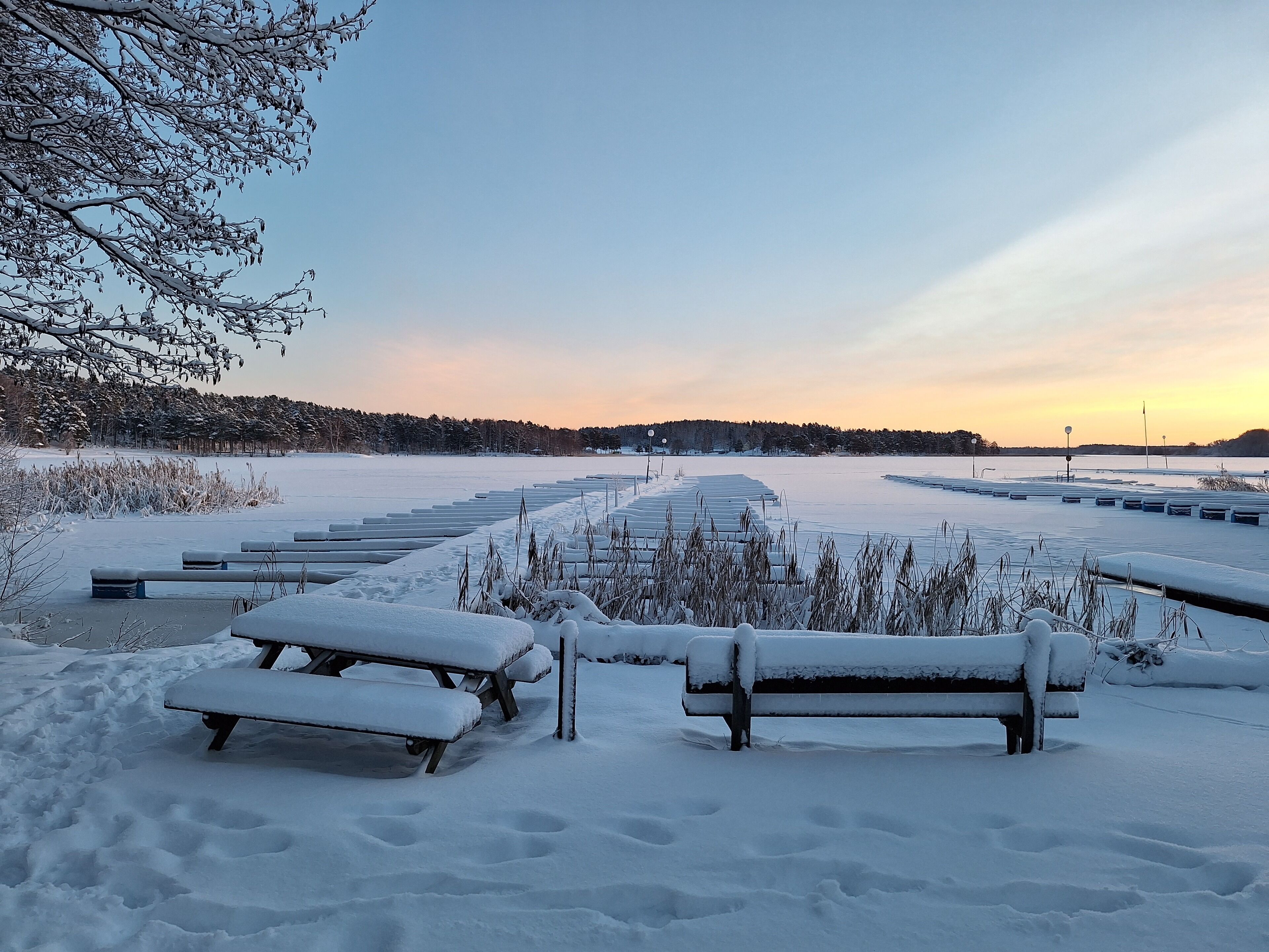 Ett snötäckt utomhusområde med bänkar och en klar himmel.
