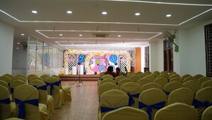 A hall with rows of yellow chairs with blue sashes, a stage with balloons and a floral backdrop, and recessed ceiling lighting. - Hotel Plaza Airport Zone (Hyderabad)