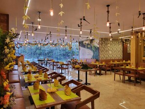 Ein Restaurant mit langen Tischen, hängenden Lampen und Wandgemälde.
