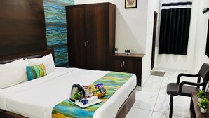 A hotel room with a large bed, a wardrobe, a small cabinet, a desk with a chair, and a window with curtains. - Hotel Plaza Airport Zone (Hyderabad)