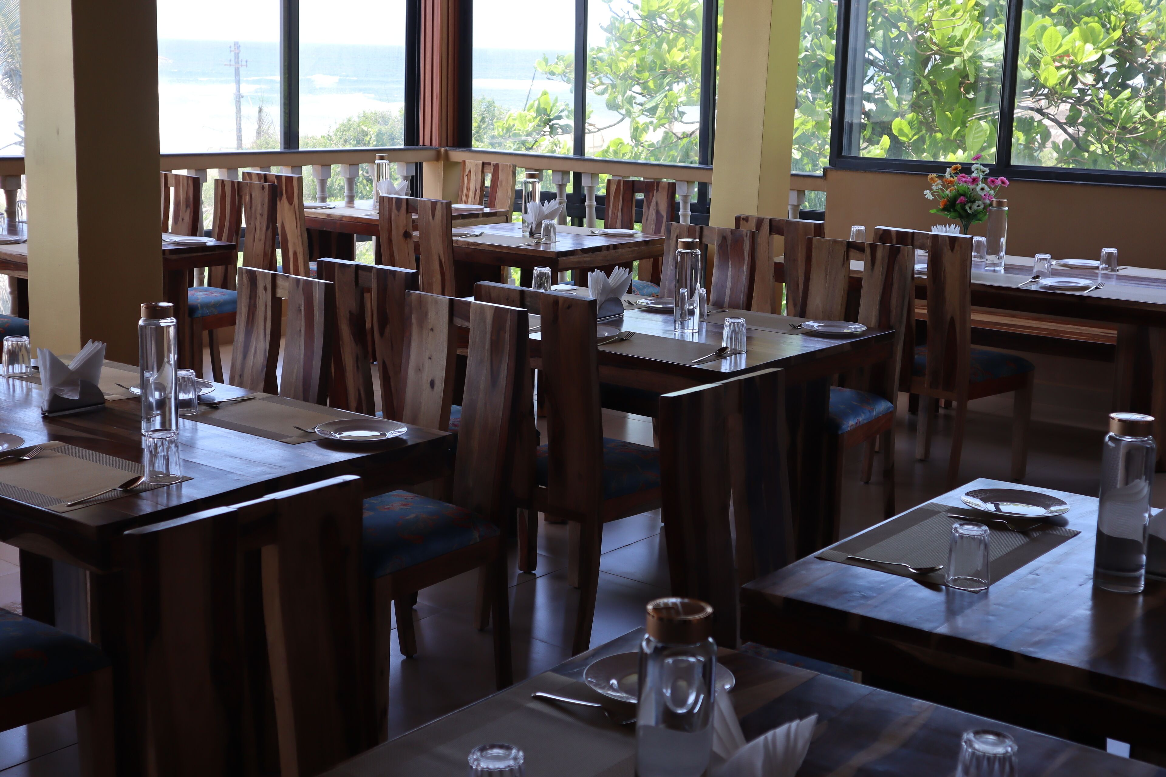 Un restaurante con varias mesas y sillas, cada conjunto con cubiertos, servilletas y botellas de agua.