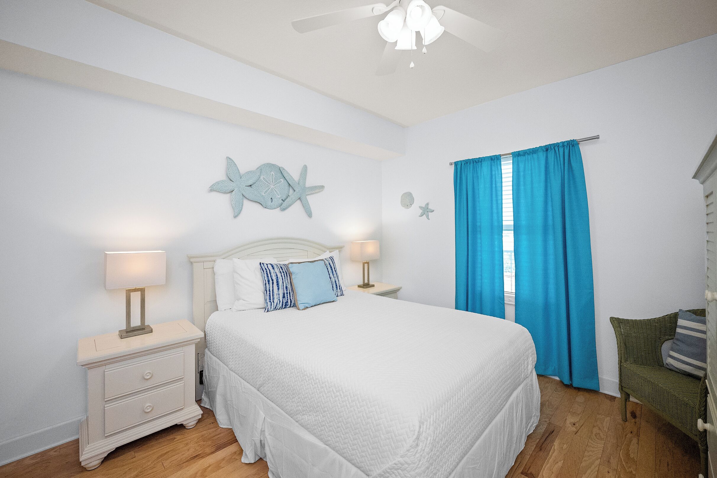 A bedroom with a bed, nightstands, a wall decoration, a window with curtains, and a ceiling fan.
