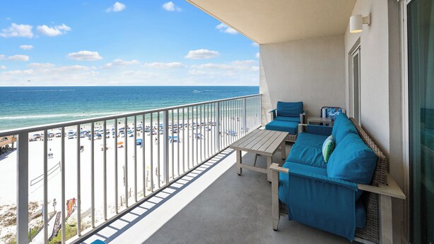 A balcony with a view of the beach and ocean, a table, and blue seating. - NEW RENTAL - Updated Beach Front - Seawind 703 - Signature Properties (Gulf Shores)