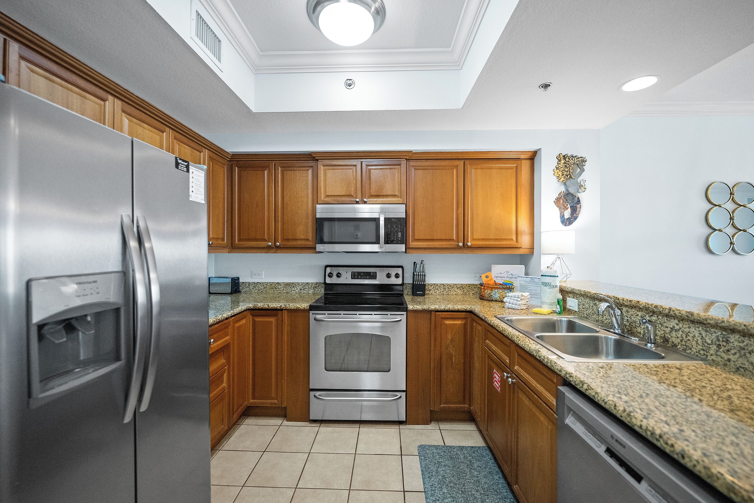 A modern kitchen with stainless steel appliances, wooden cabinets, granite countertops, and a built-in oven.