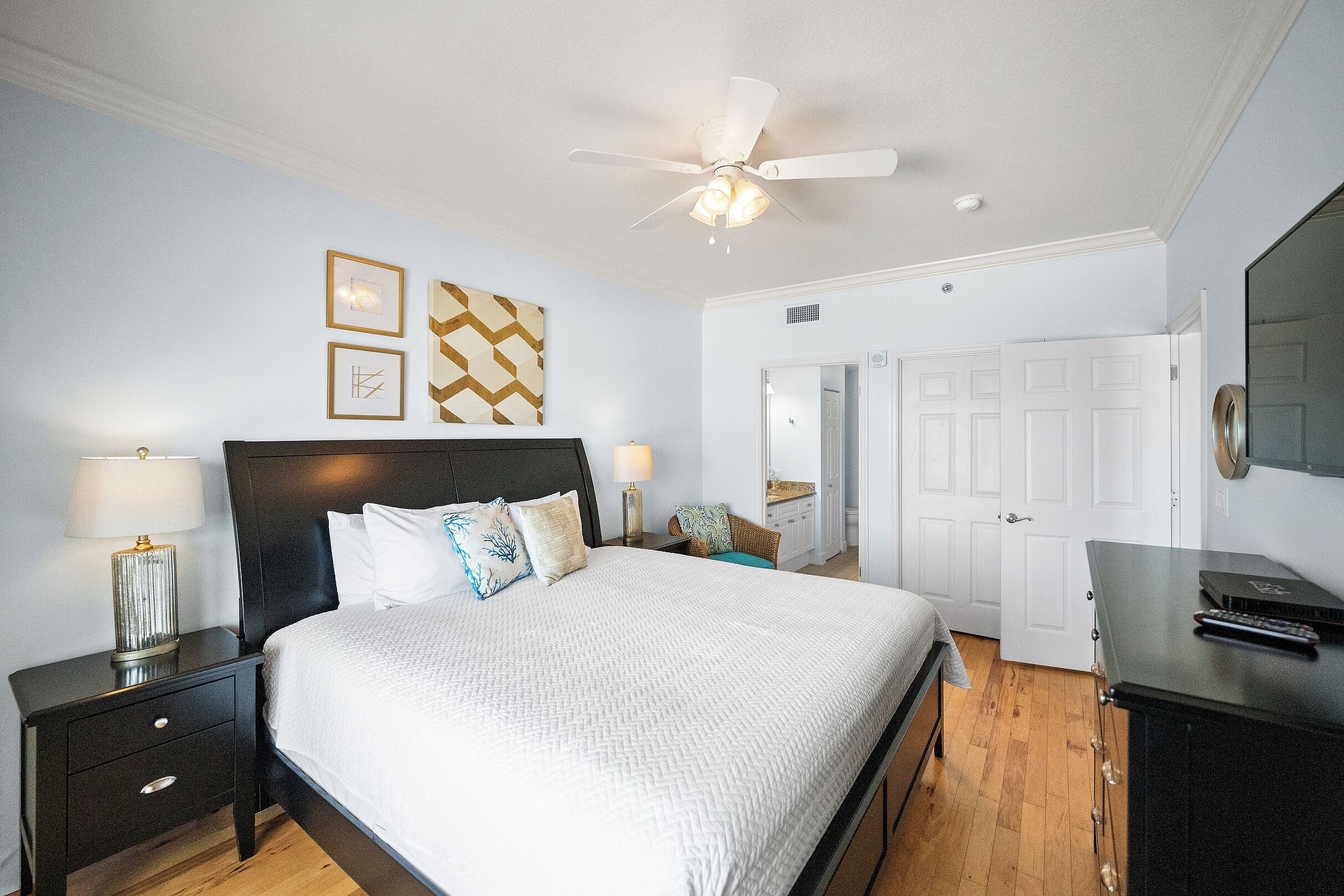 Une chambre à coucher comprenant un lit, des tables de chevet, un ventilateur de plafond et une commode.