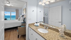A hotel room with a bed, a bathroom with a sink and mirror, and a view of the ocean. - NEW RENTAL - Updated Beach Front - Seawind 703 - Signature Properties (Gulf Shores)