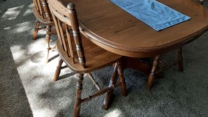 A dining area with a wooden table, chairs, and a blue placemat. There is a brown sofa and a lamp in the background. - Trillium Bed & Breakfast (Niagara Falls)