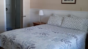 A bedroom with a bed, a nightstand, a lamp, a framed picture on the wall, and a door leading to a bathroom. - Trillium Bed & Breakfast (Niagara Falls)