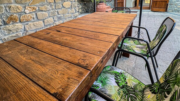 Eine rustikale Steinmauer, ein Holztisch und Metallstühle mit tropischem Muster.