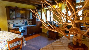 Eine rustikale Küche mit Holzschnitzereien, einem Esstisch mit einem Blumenmuster auf der Tischdecke und einer großen Holzskulptur.