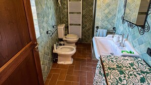 Ein Badezimmer mit Holztür, einer Dusche mit weißem Handtuchhalter, einer Toilette mit rosa Handtuch und einem Waschbecken mit grünem Seifenspender.