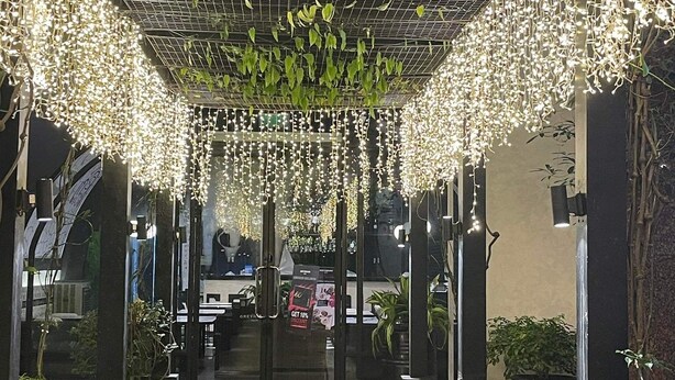 Een binnentuin met hangplanten en verlichting, stenen zuilen en een betegelde vloer.