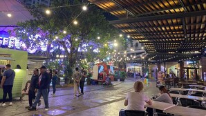 Een terras met tafels en stoelen, omgeven door bomen en lichtjes.