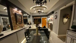 Een moderne keuken met een glazen eettafel, witte kasten en een wand met stenen accenten.