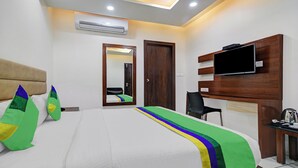 Habitación de hotel con cama, televisor montado en la pared, escritorio y equipo de aire acondicionado.