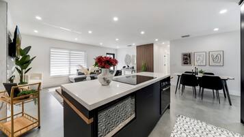 Une cuisine moderne dotée d’un îlot central, un coin repas avec une table et des chaises noires, et un espace de vie comprenant un canapé et une table basse.
