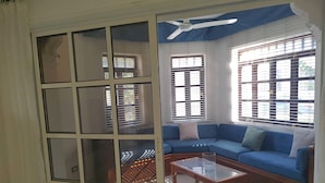 A living room with a blue sofa, a glass coffee table, and a ceiling fan. - Stunning Spacious One Bed in Delta Sharm (Sharm El Sheikh)