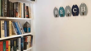 A bookshelf with various books and a decorative wall hanging spelling "BEACH". - Stunning Spacious One Bed in Delta Sharm (Sharm El Sheikh)