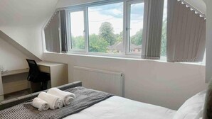Ein Schlafzimmer mit einem großen Bett, einem Schreibtisch und einem Fenster mit Vorhängen.