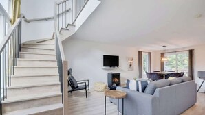 A modern living room with a staircase, a fireplace, a sofa, and a dining area. - Cerf Blanc | Sauna & Piscine by Alchalet (Pont-Rouge)