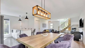 A modern interior with a dining area, kitchen, and living space, featuring a staircase and a TV.