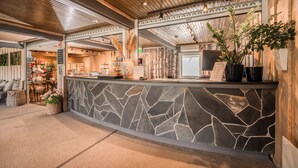 Un área de recepción con mostrador de piedra, techo de madera y plantas en macetas.