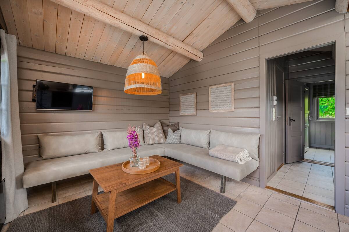 A modern living room with a wooden ceiling, a sectional sofa, a wooden coffee table, and a television mounted on the wall.