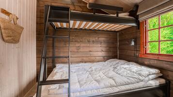 Una cama litera con escalera, una ventana con vistas a la vegetación y un bolso tejido en la pared.