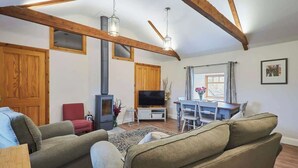 Una sala de estar acogedora con chimenea, vigas de madera, televisor y comedor.