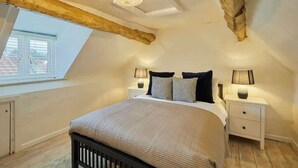 A bedroom with a sloped ceiling, a skylight, a bed with a headboard, two bedside tables with lamps, and a window with blinds. - Host & Stay | Cragg Cottage (Whitby)