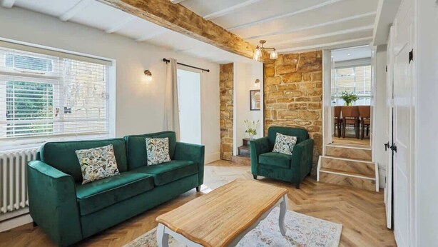 A spacious living room with a green sofa, a wooden coffee table, and a stone wall. - Host & Stay | Cragg Cottage (Whitby)