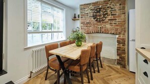 A dining area with a brick wall, a wooden table, and brown chairs. - Host & Stay | Cragg Cottage (Whitby)