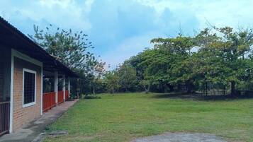 A covered outdoor area with a brick building, a grassy lawn, and trees.