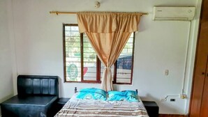 Een slaapkamer met een bed, een zwarte bank, een raam met gordijnen en een airconditioning.