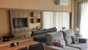 Una sala de estar moderna con un sofá, una mesa de comedor con sillas, un televisor de pantalla plana en la pared y un ventanal con cortinas.